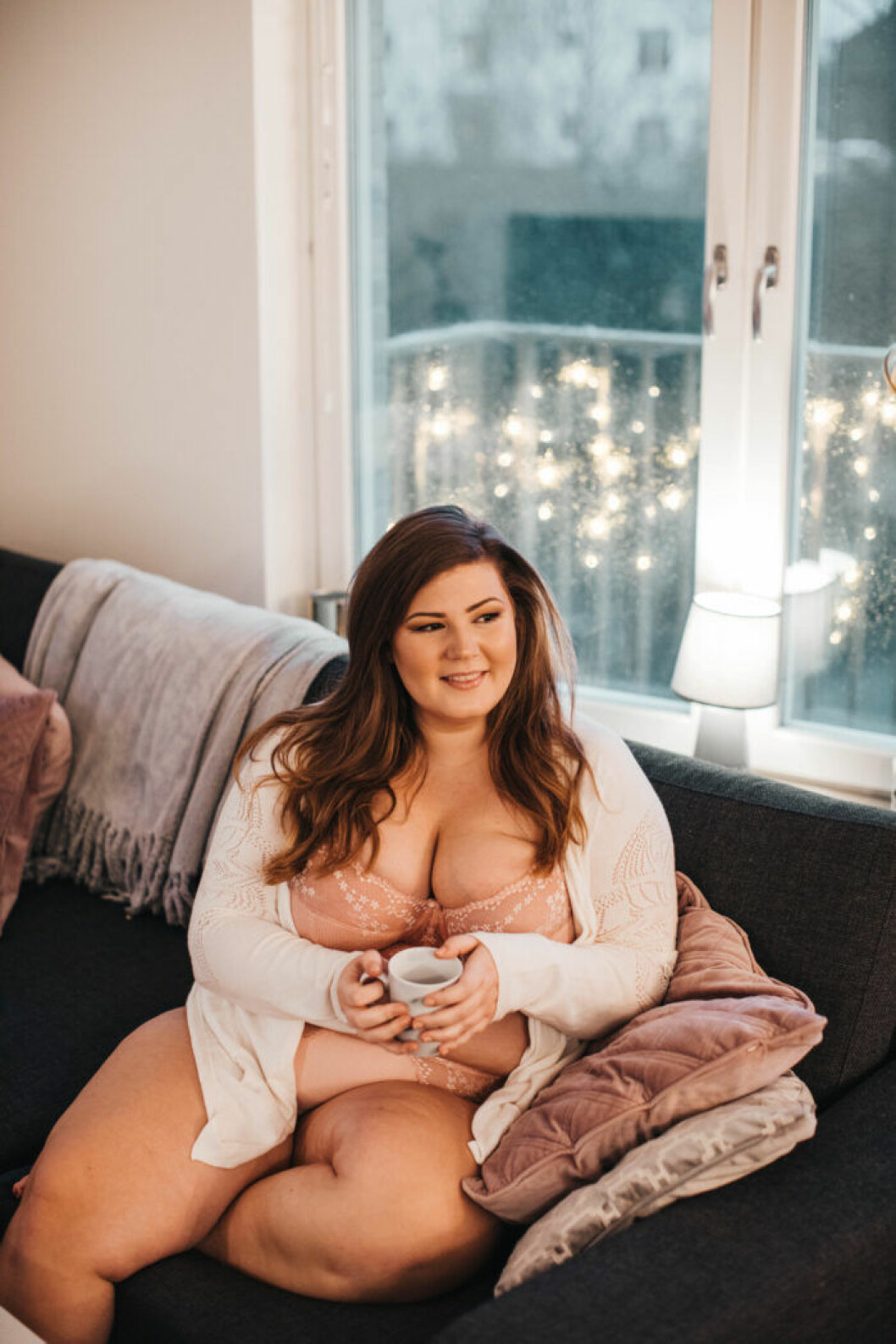 Influencern Linda-Marie tipsar om att gå runt avklädd hemma för att bli mer kroppspositiv. Kroppen är inte sämre med kläder än avklädd. Foto: Evelina Sigetty Kroppspositivisten Linda-Marie sitter i en soffa med en kopp.