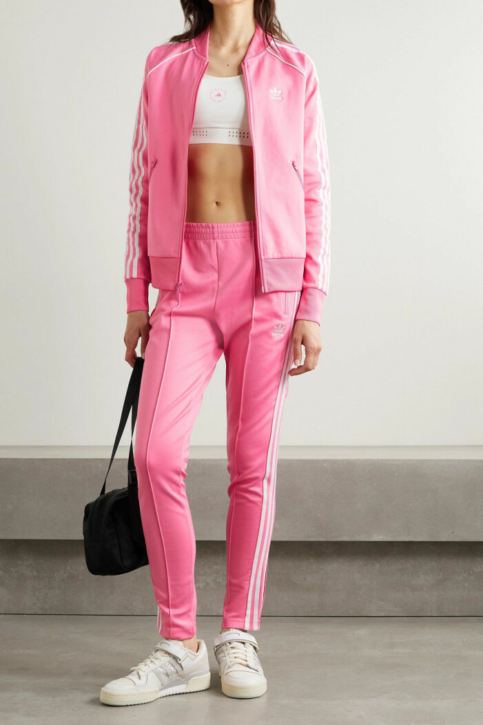 Tracksuit, Adidas. <a target="_blank" rel="nofollow" href="https://www.net-a-porter.com/en-us/shop/product/adidas-originals/sport/jackets/adicolor-superstar-striped-cotton-blend-satin-jersey-track-jacket/11452292645283594">Klicka på bilden för att komma direkt till produkterna!</a> Modell med rosa tracksuit i jersey. Jacka och byxa med klassiska vita Adidas-ränder på ärmar och ben. Under tracksuiten har modellen en vit sporttopp. Set från Adidas.