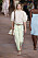 Modell med blus med hög volangkrage och puffärmar. Till det ett par batikfärgade jeans i ljusgult och grönt. Virkad väska och brunt bälte i midjan och reptofflor på fötterna. Look från Alberta Ferretti ss21.