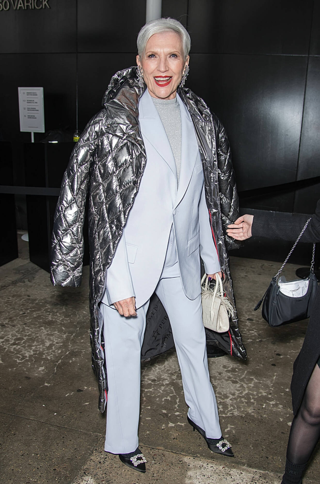 Maye Musk bär klassisk kostym som matchas med silverfärgad kappa.
