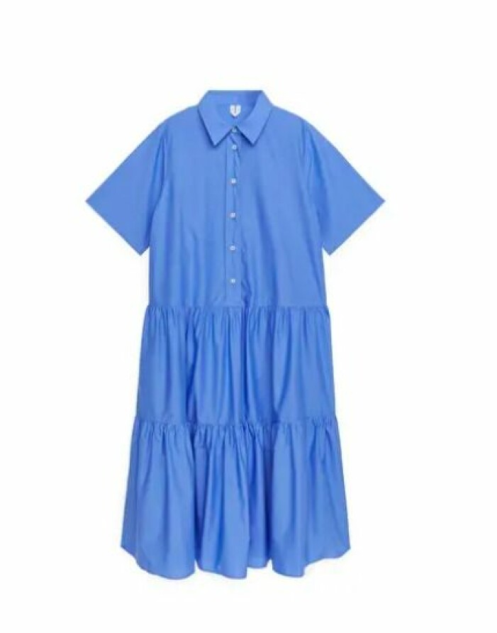Klarblå skjortklänning med korta, vida ärmar och knappar. Så kallad däckmönstrad nertill, volangliknande. Klänning från Arket.