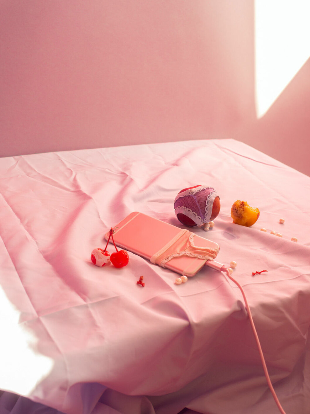 En av Arvida Byströms installationer på Fotografiska. Foto: Fotografiska Frukter i stringtrosor på ett rosa bord under Arvida Byströms utställning Inflated Fiction.