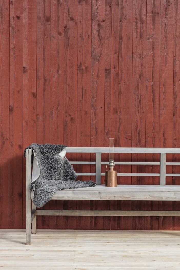 På verandan en vacker träbänk, fårskinn och lykta från Klong. Attefallshus Sommarnöje GAD Gotland bänk lykta Klong