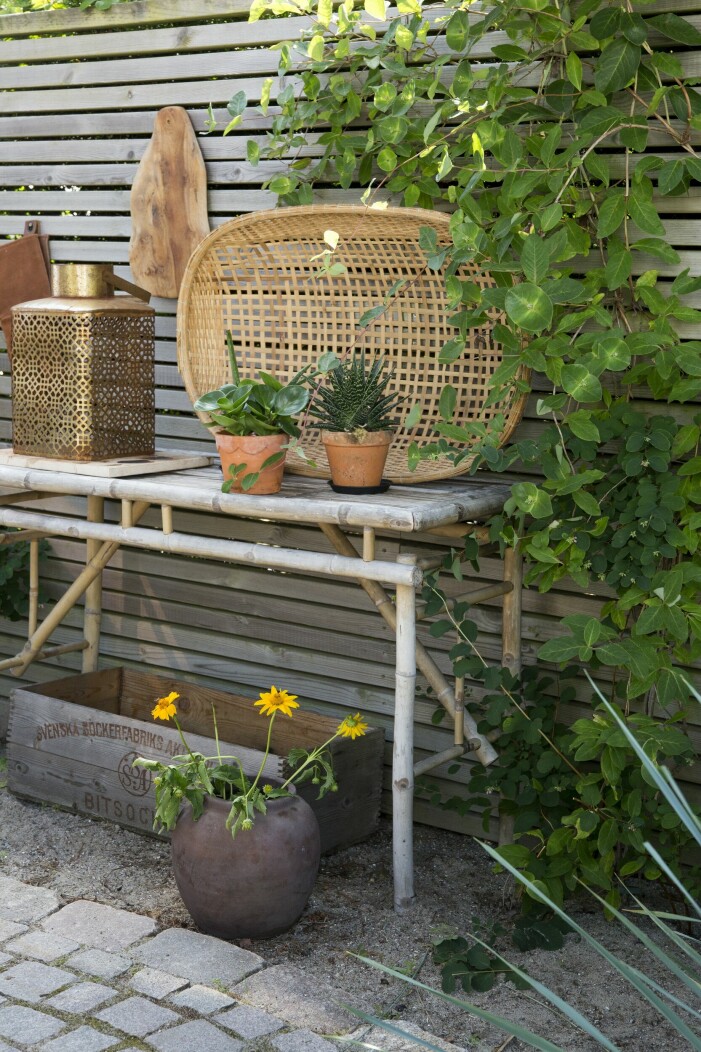 Strax intill matbordet står ett sideboard i bambu, en gåva från en väninna. På staketet bakom klättrar en vildkaprifol som Maria har planterat. Korgfat från Barkåkra Trädgårdsmöbler. Mässingslykta från Closet & House, Nykvarn. Intill matplatsen finns ett bord i bambu.