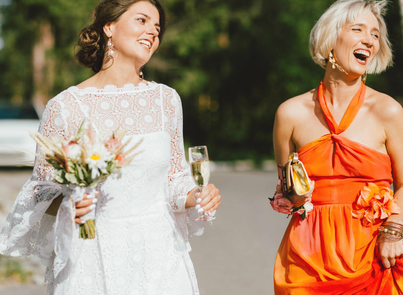 Vit brudklänning i spets och bröllopsgäst i färgstark festklänning.