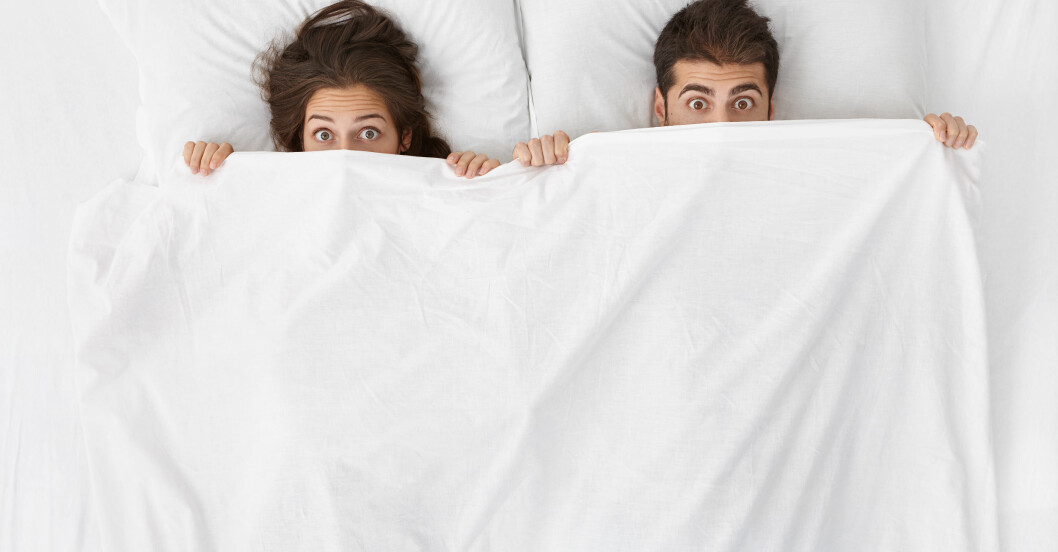 Brunhårig kvinna och man under täcke i säng