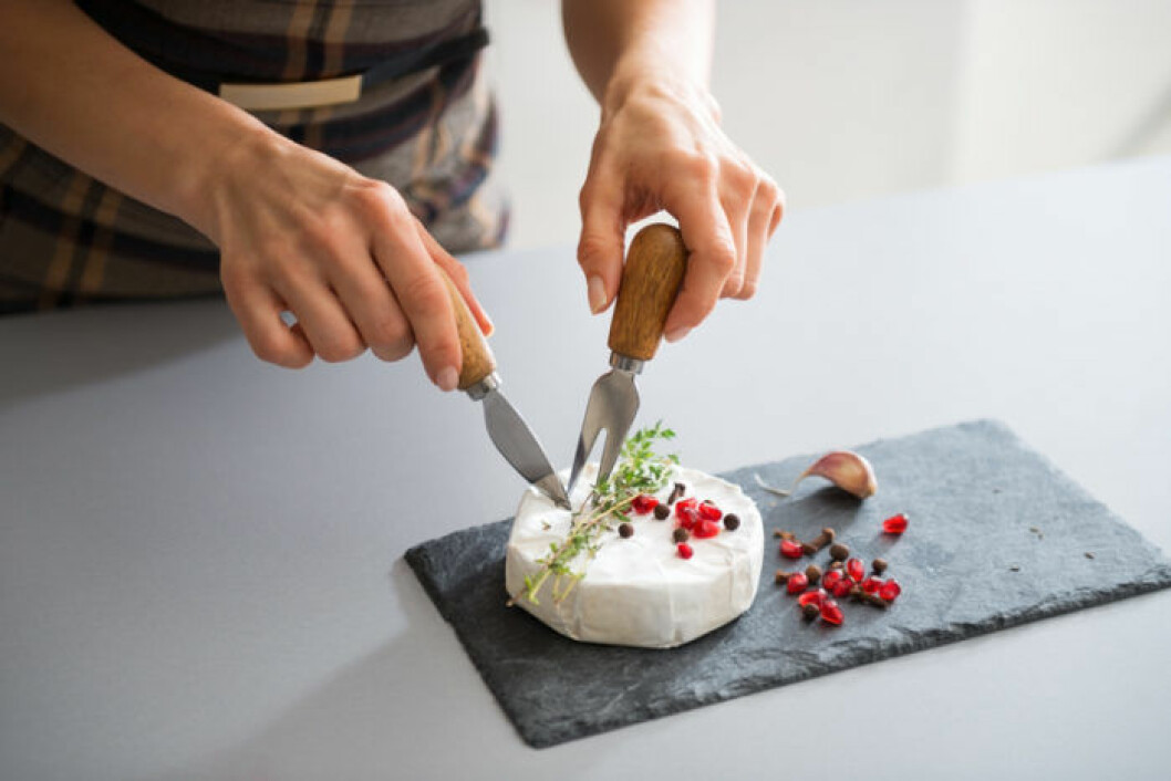 Camembert. Bild: Shutterstock/IBL Kvinna skär upp en camembert.