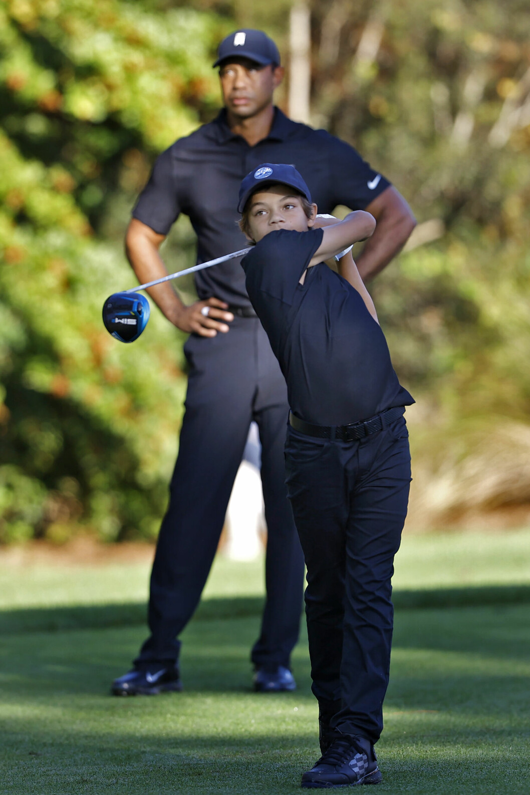 Pappa Tiger tittar på när Charlie Woods svingar klubban. charlie woods svingar golfklubban