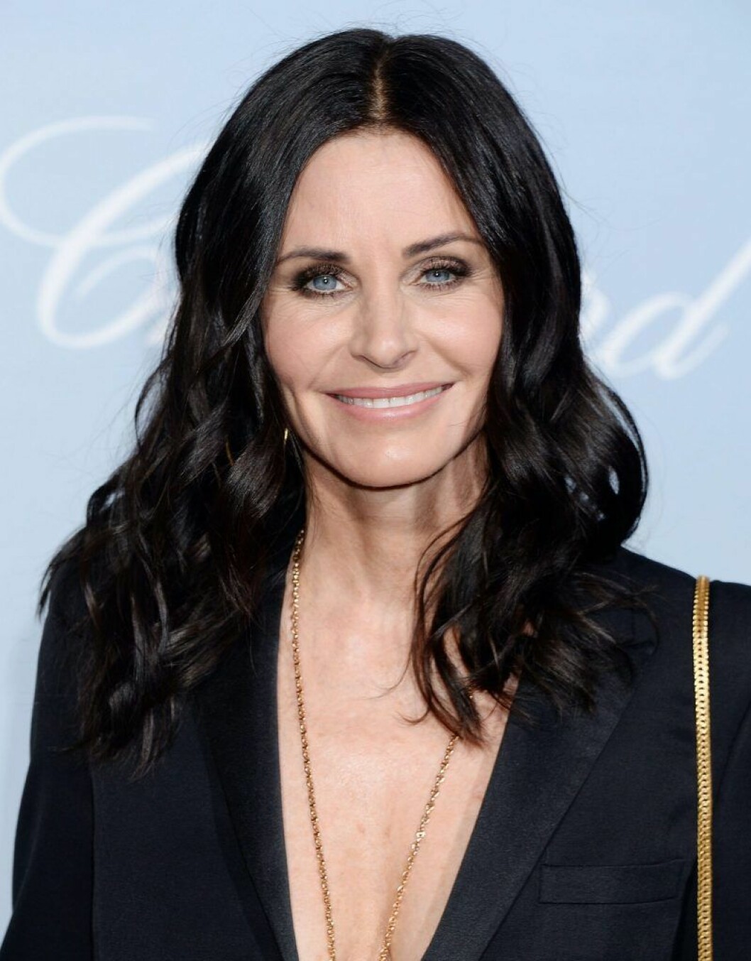 Courteney Cox spelade Monica. Courteney Cox ler i svart kostym och utsläppt hår