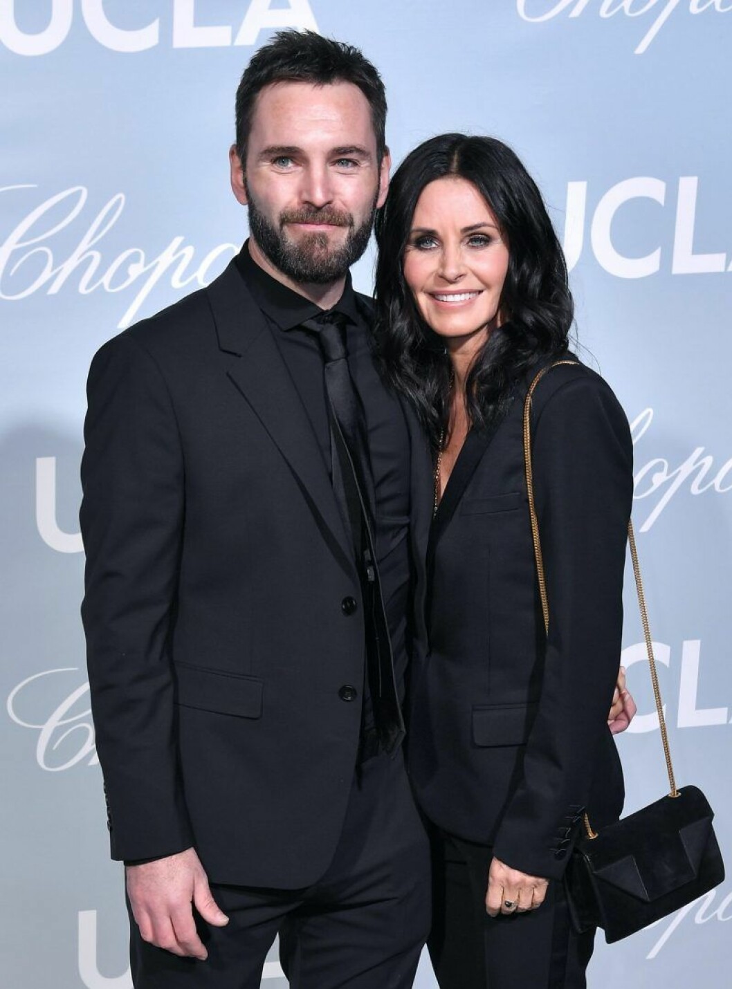 Courteney Cox och Johnny McDaid. Courteney Cox och Johnny McDaid är svartklädda och ler