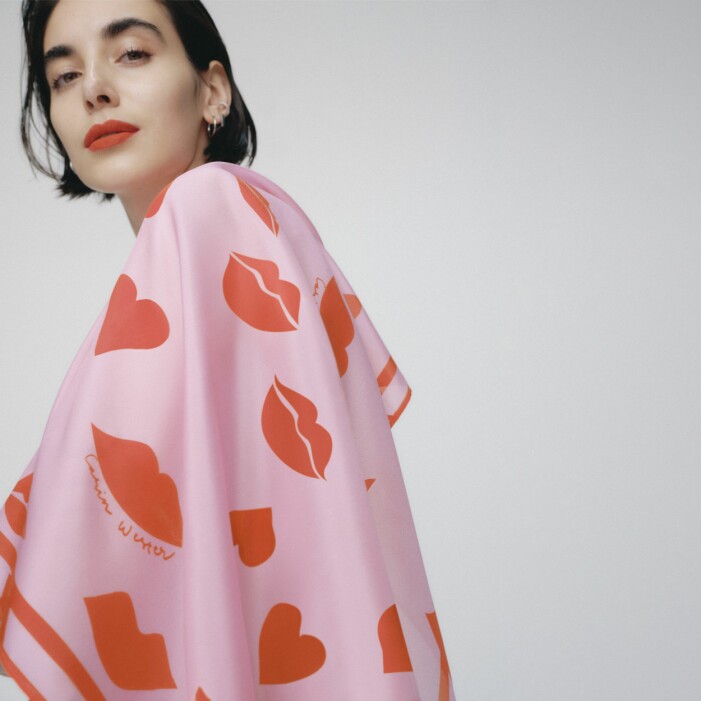 Tanken var att designa en scarf som "poppar". Scarfen passar utmärkt till höstrocken eller som en färgglad detalj på handväskan. <a target="_blank" rel="nofollow" href="https://in.ahlens.se/t/t?a=1136856392&as=1218462148&t=2&tk=1&epi=an-cwscarf&url=https://www.ahlens.se/Mode/accessoarer/halsdukar-scarves-15213/carin-wester-scarf-heart-lips-onesize-pink-multi-61011587/">Klicka på bilden för att komma direkt till produkten!</a> Modell med scarfen designad av Carin Wester över axlarna. Scarfen är rosa med röda läppar och hjärtan på.