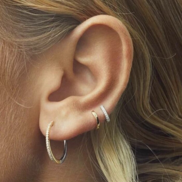 Örhängen, Ennui Atelier. Tre örhängen fotade på ett öra. En större ring med diamanter och två mindre hoops, en slät i guld och en med diamanter. Örhängen från Ennui Atelier.