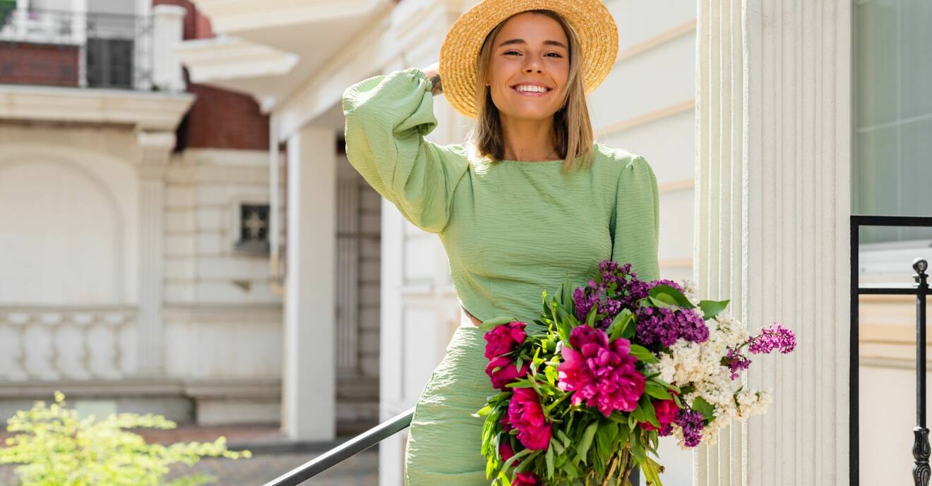Glad kvinna med blommor och hatt.