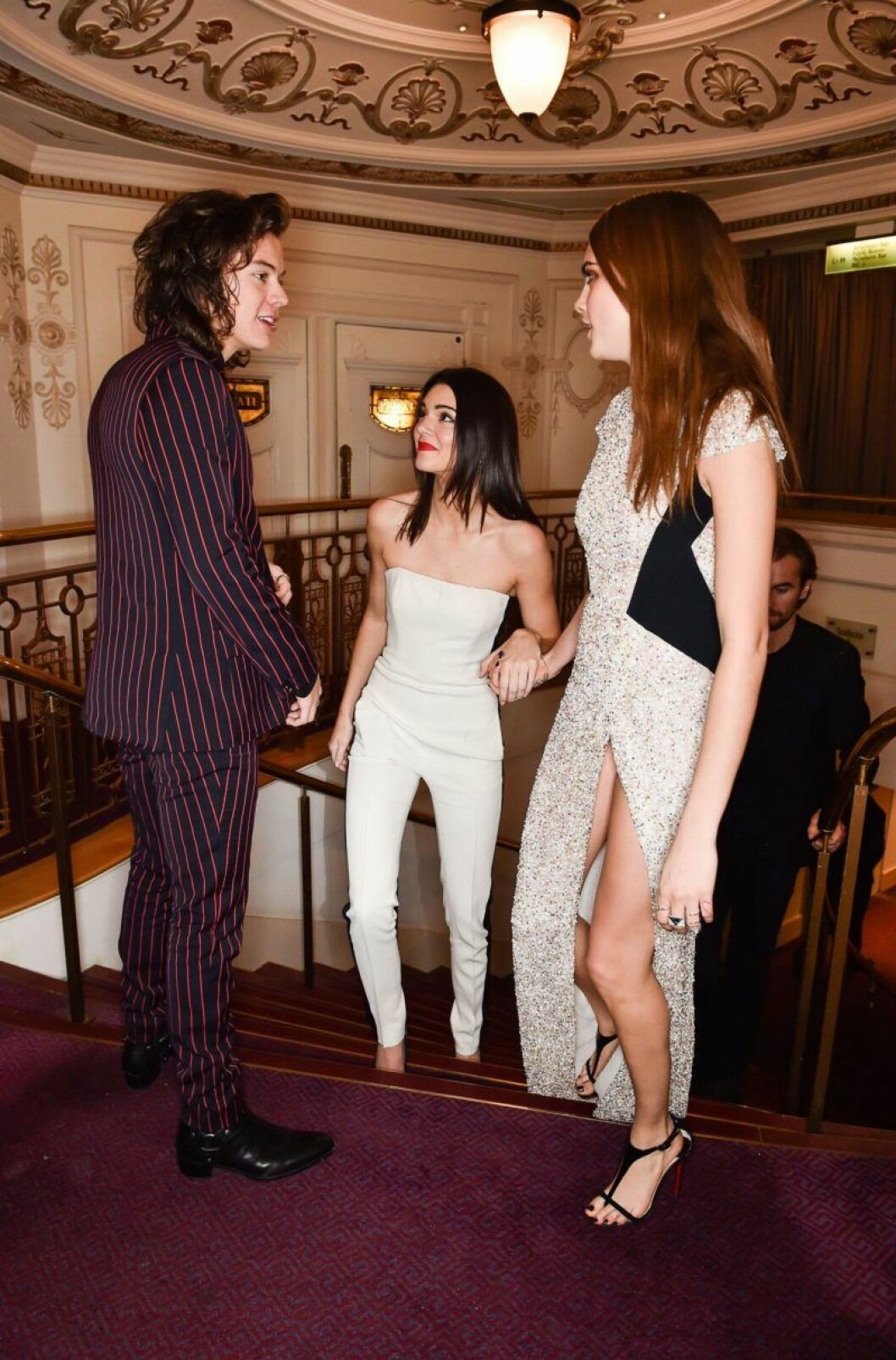 Kendall Jenner kunde knappt hålla sig för skratt under det något märkliga mötet med både sitt och Cara Delevingnes ex Harry Styles. Harry Styles, Kendall Jenner och Cara Delevingne står i en trappa