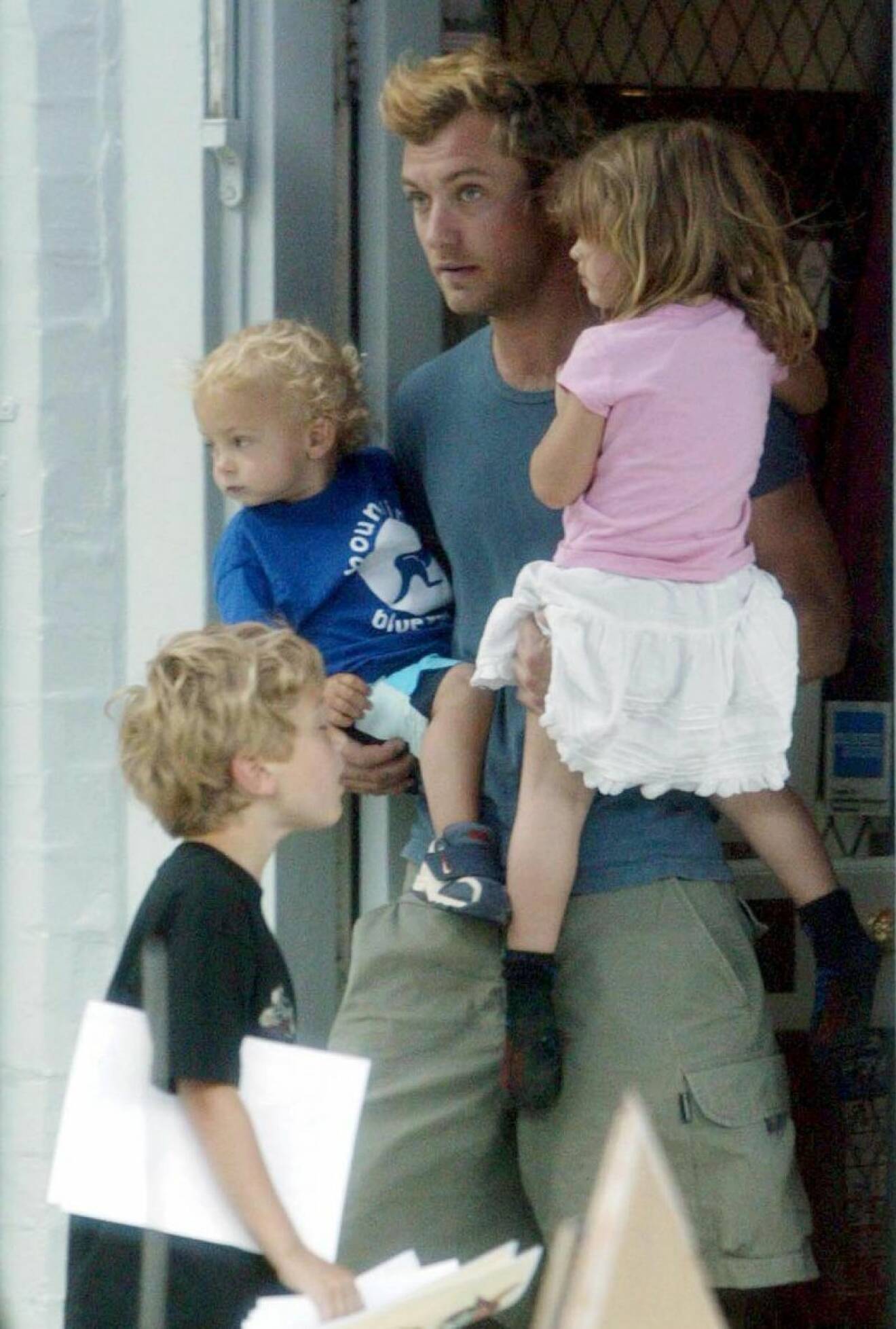 Jude law bär två barn och ett barn står framför honom