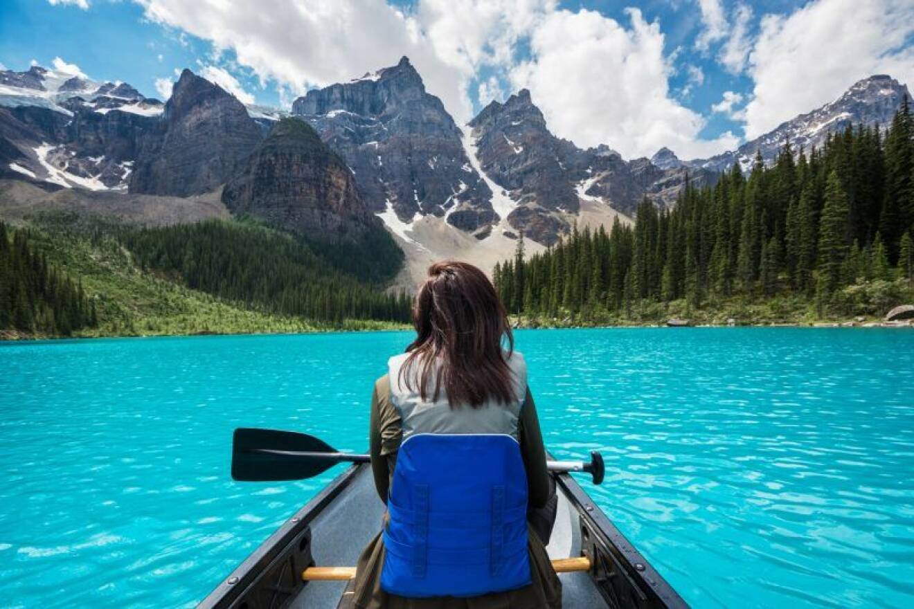 Kvinna paddlar kanot på sjö bland bergen i Kanada