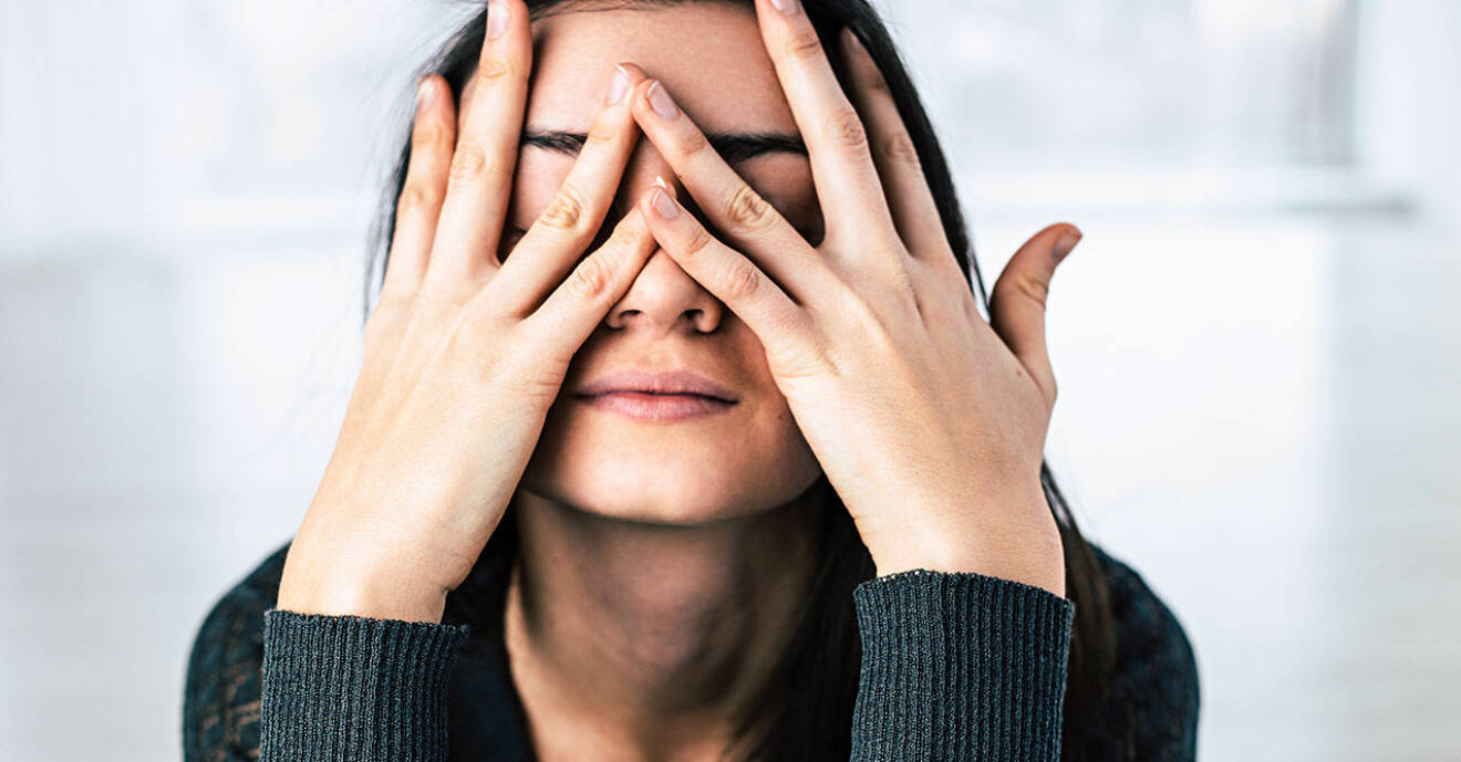 Stressad kvinna med mörkt hår gömmer ansiktet i händerna