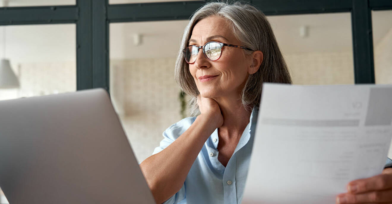 en kvinna med grått hår och glasögon tittar i papper och på sin dator