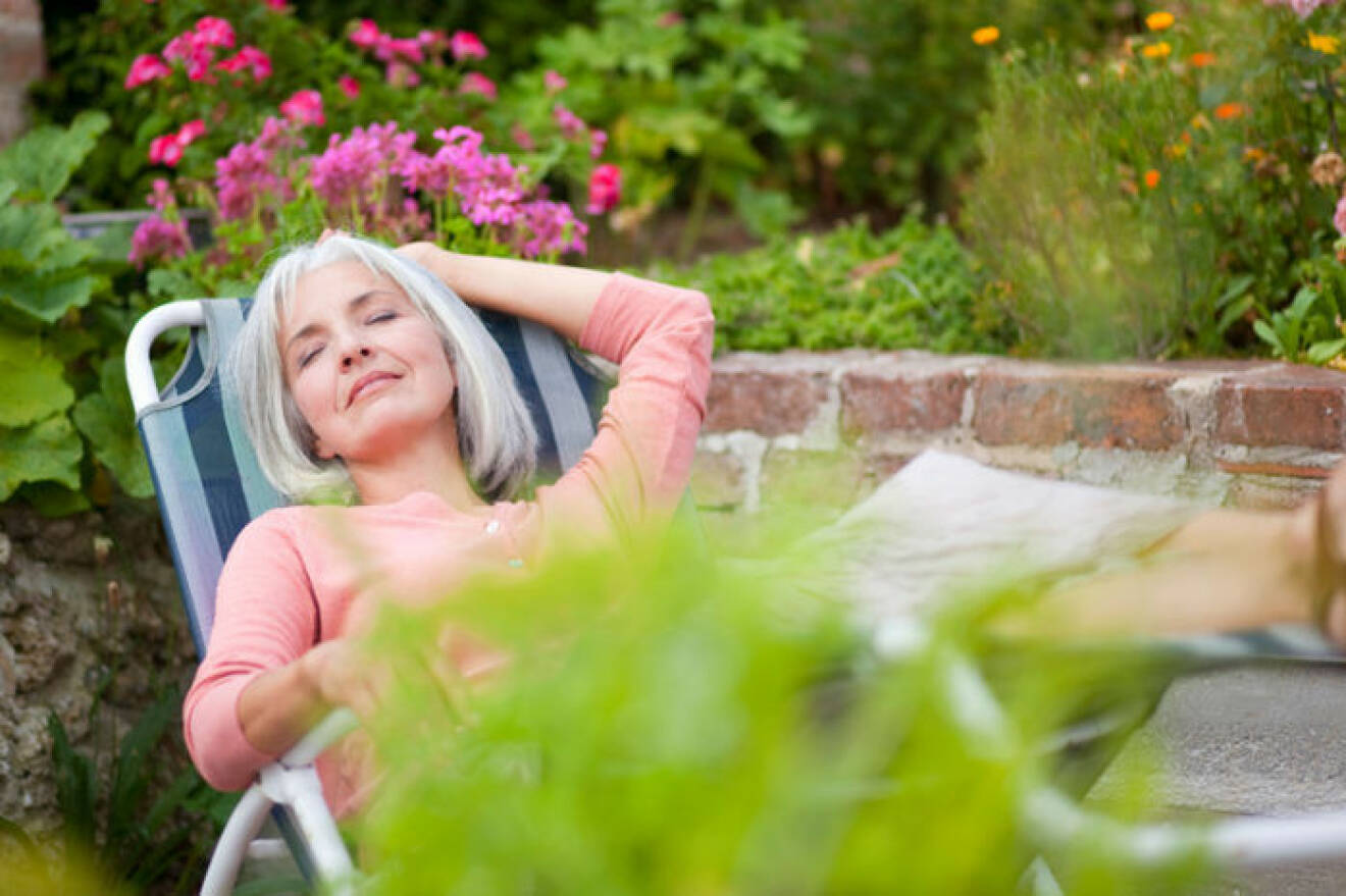 Kvinna sover i solstol i trädgård.