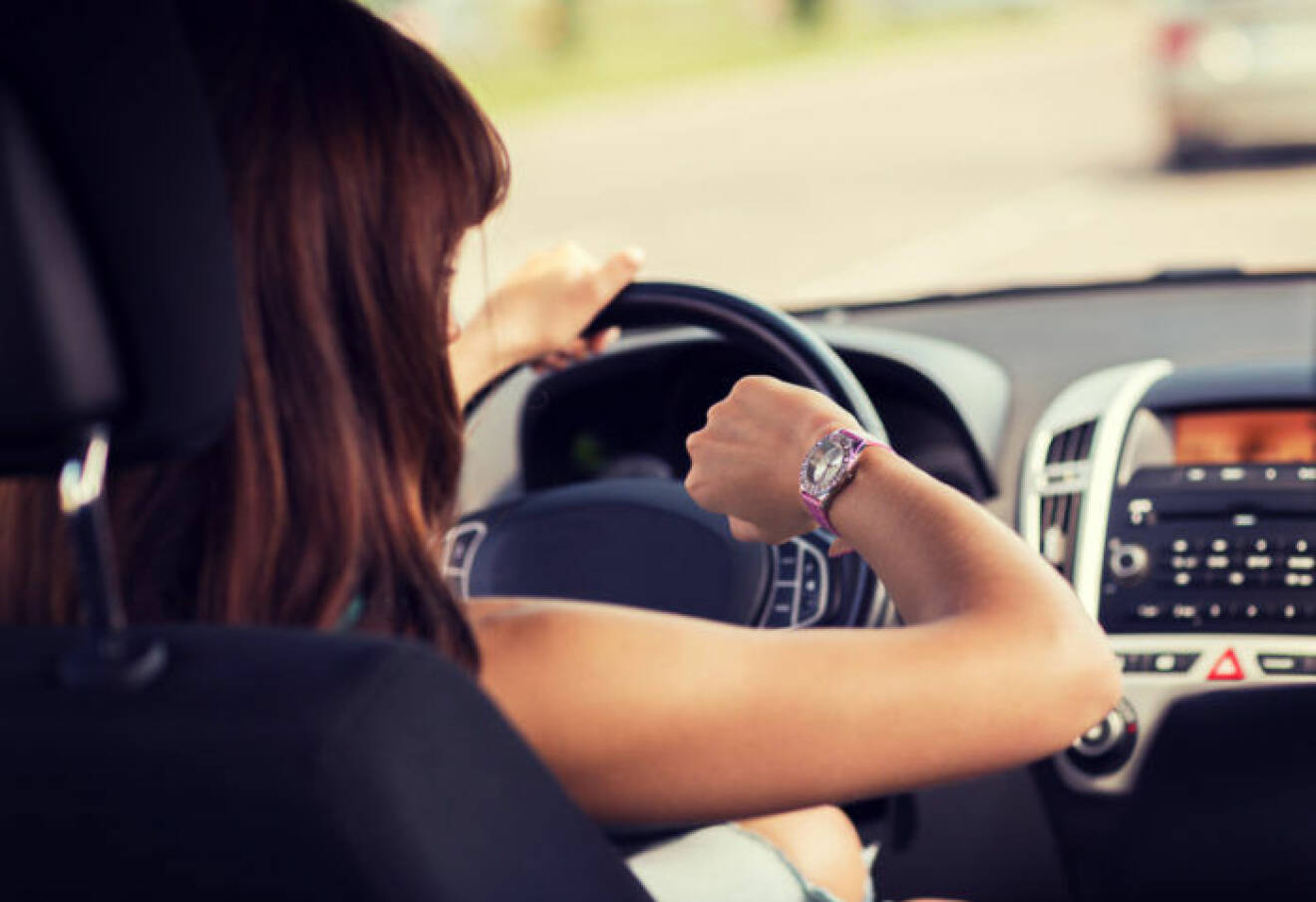Stressad kvinna kör bil och tittar på sitt armbandsur.