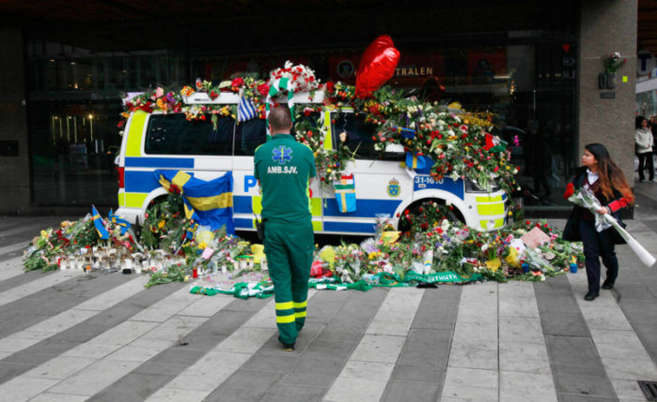 Drottninggatan i Stockholm april 2017. En målad polisbil täckt med blommor. Framför står en ambulanssjukvårdare och tittar på polisbilen.