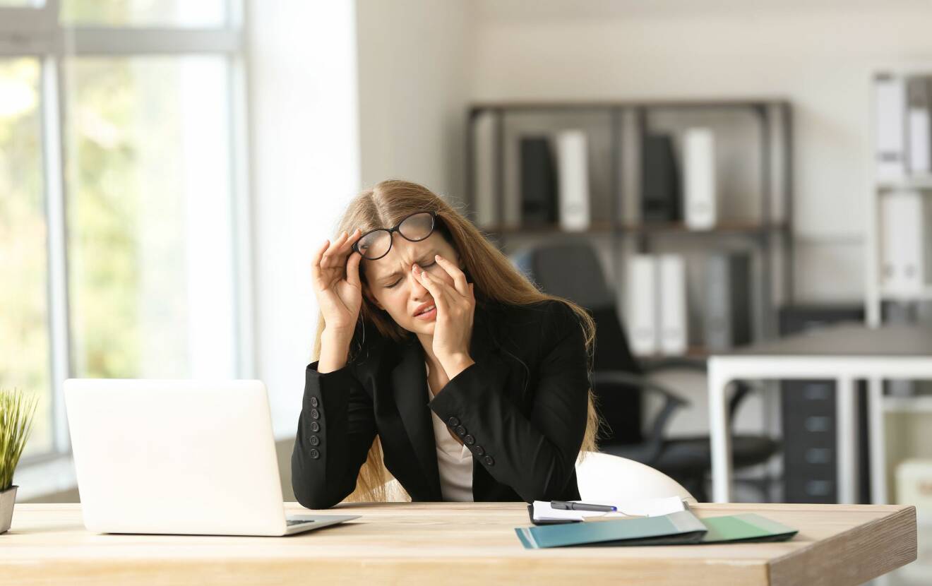 Kvinna vid dator med huvudvärk.