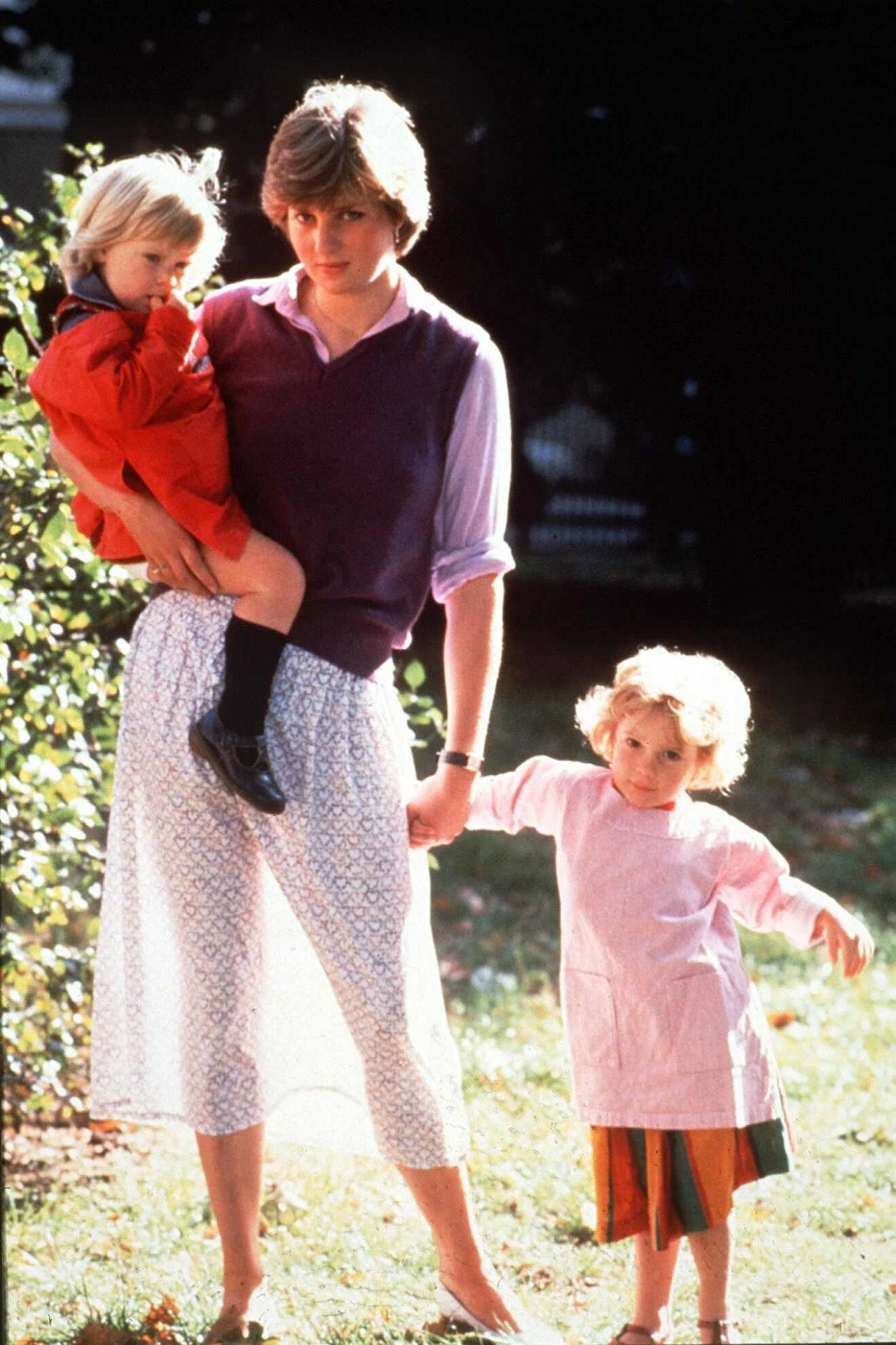 Prinsessan Diana i en skir maxikjol. I famnen bär hon ett barn och hon håller ett annat barn i andra handen. Bilden är tagen 1980 på förskolan där hon jobbade på innan hon gifte sig med Prins Charles.