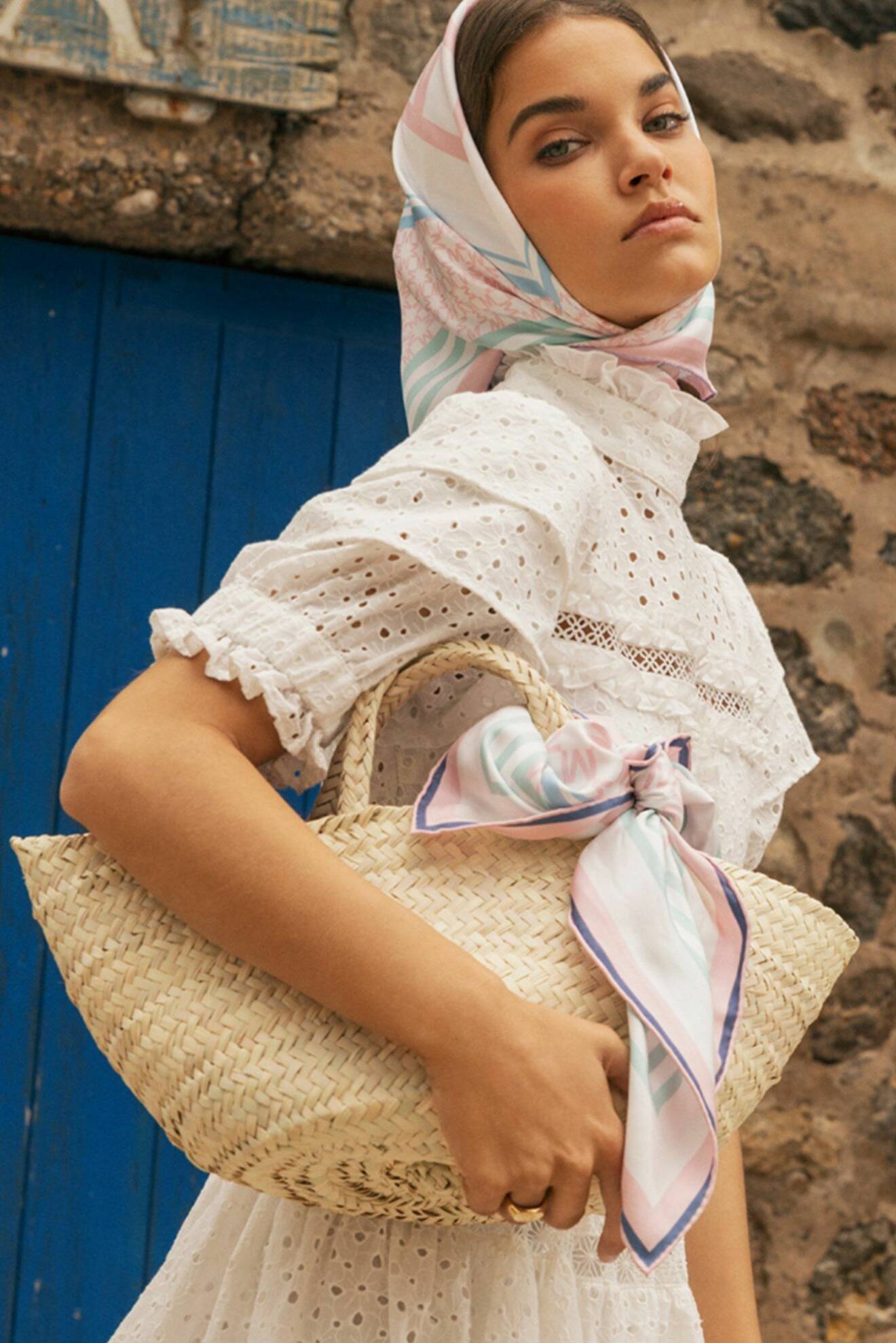 Modell med scarf runt huvudet och knuten runt stråväskan. Scarf i vitt och pasteller från By Malina.