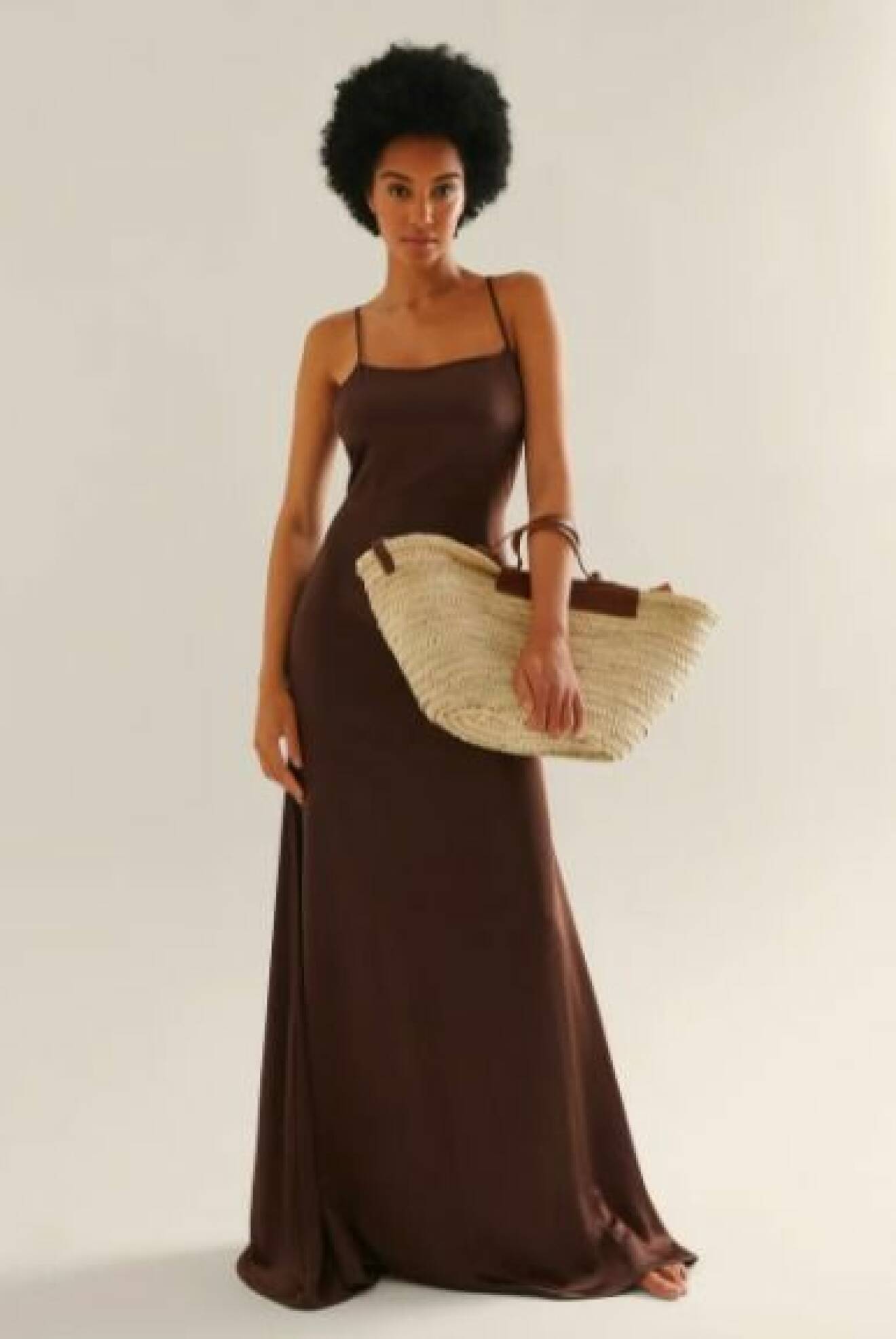 Modell med brun maxiklänning och en stråväska med bruna detlajer i skinn