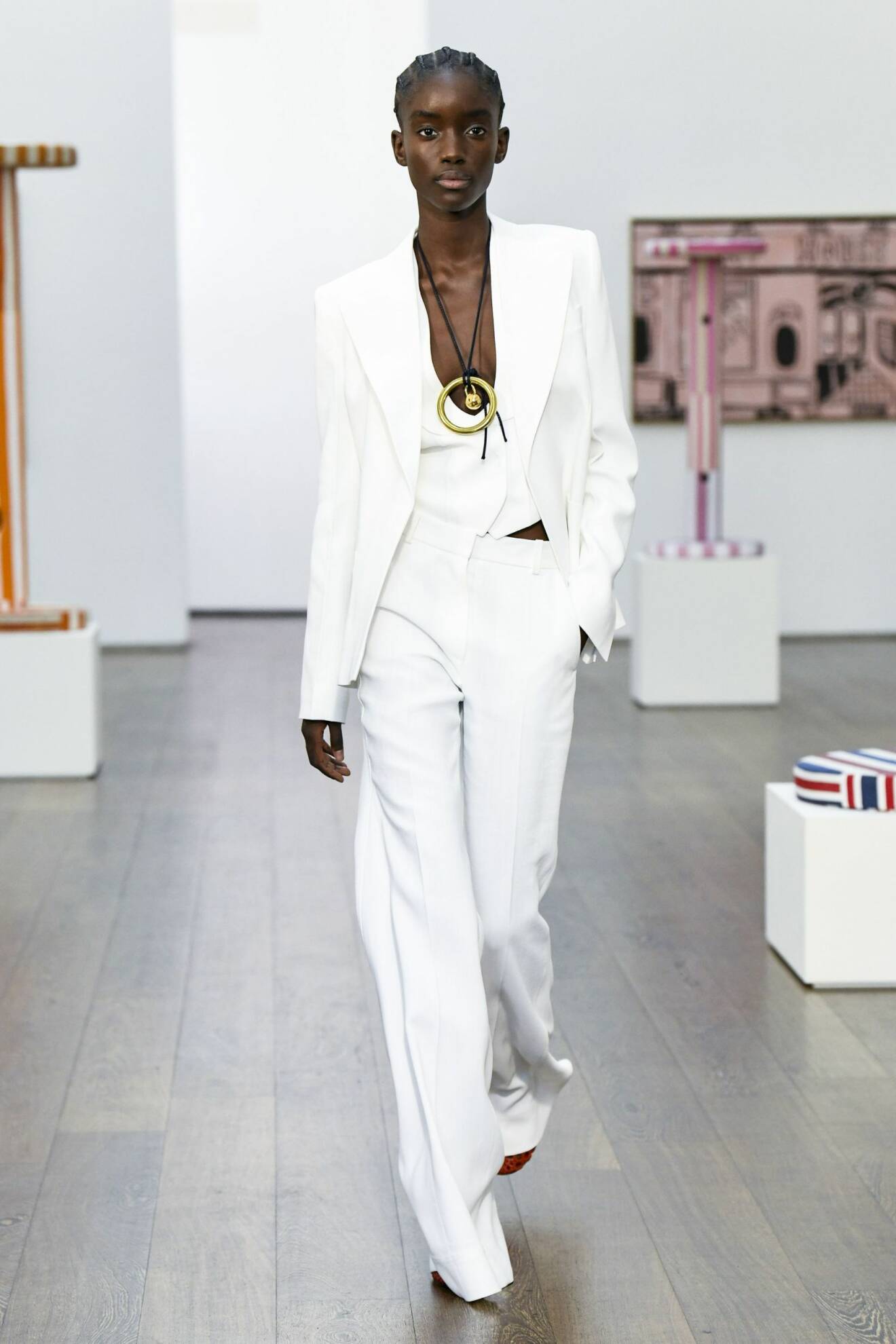 Modell med vit kostym och väst under kavajen och långa dressade byxor. Allt i vitt. Look från Victoria Beckham.