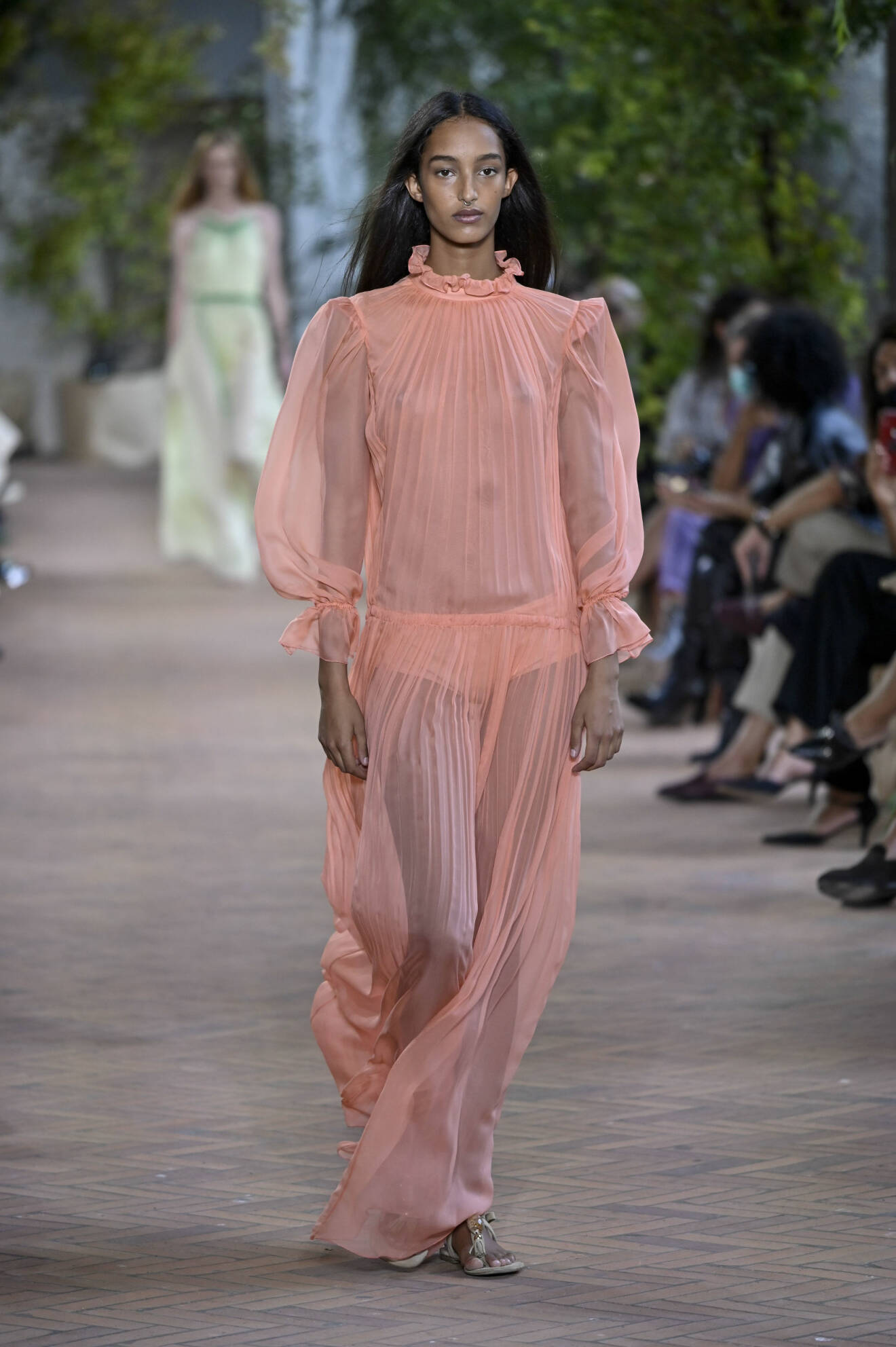 Modell med rosa-aprikos maxiklänning med volang vid halsen och plisserade detaljer. Look från Alberta Ferretti ss21.