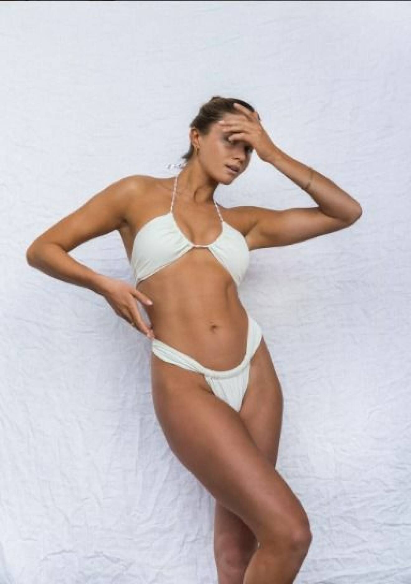 Modell med vit bikini i liggande trekantsmodell och trosor med draperat och knutar i sidorna. Bikini från Seaquelle.