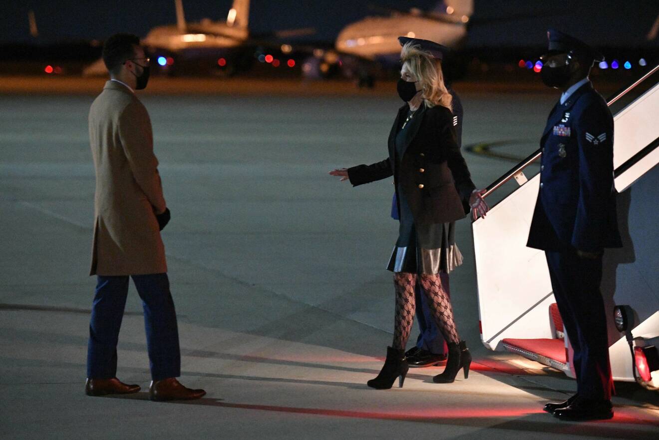 Jill Biden kommer ur ett flygplan. Hon har svart munskydd, svart kavaj och svart kjol, vad som ser ut som mönstrade, transparenta strumpbyxor och svarta ankelboots med klack.
