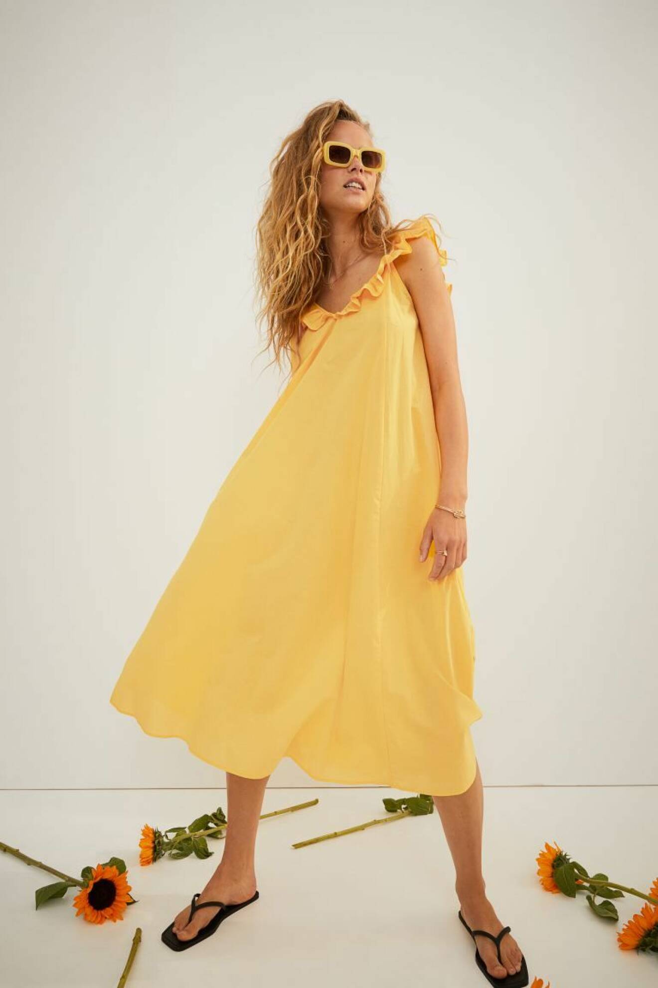 Modell med gul sommarklänning i midimodell med volangdetalj som axelband. Vid klänning från H&amp;M.