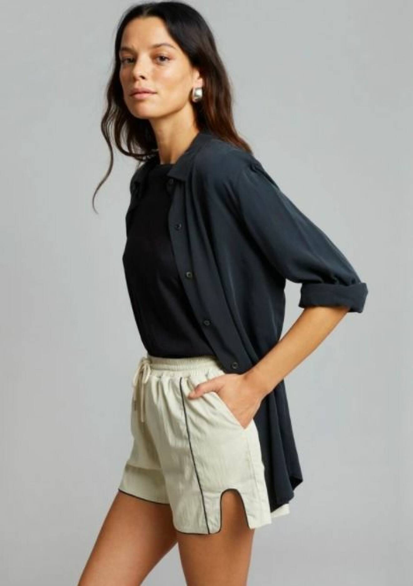 Modell med svart skjorta och korta, beige shorts i sportig modell. Outfit från The Frankie shop.