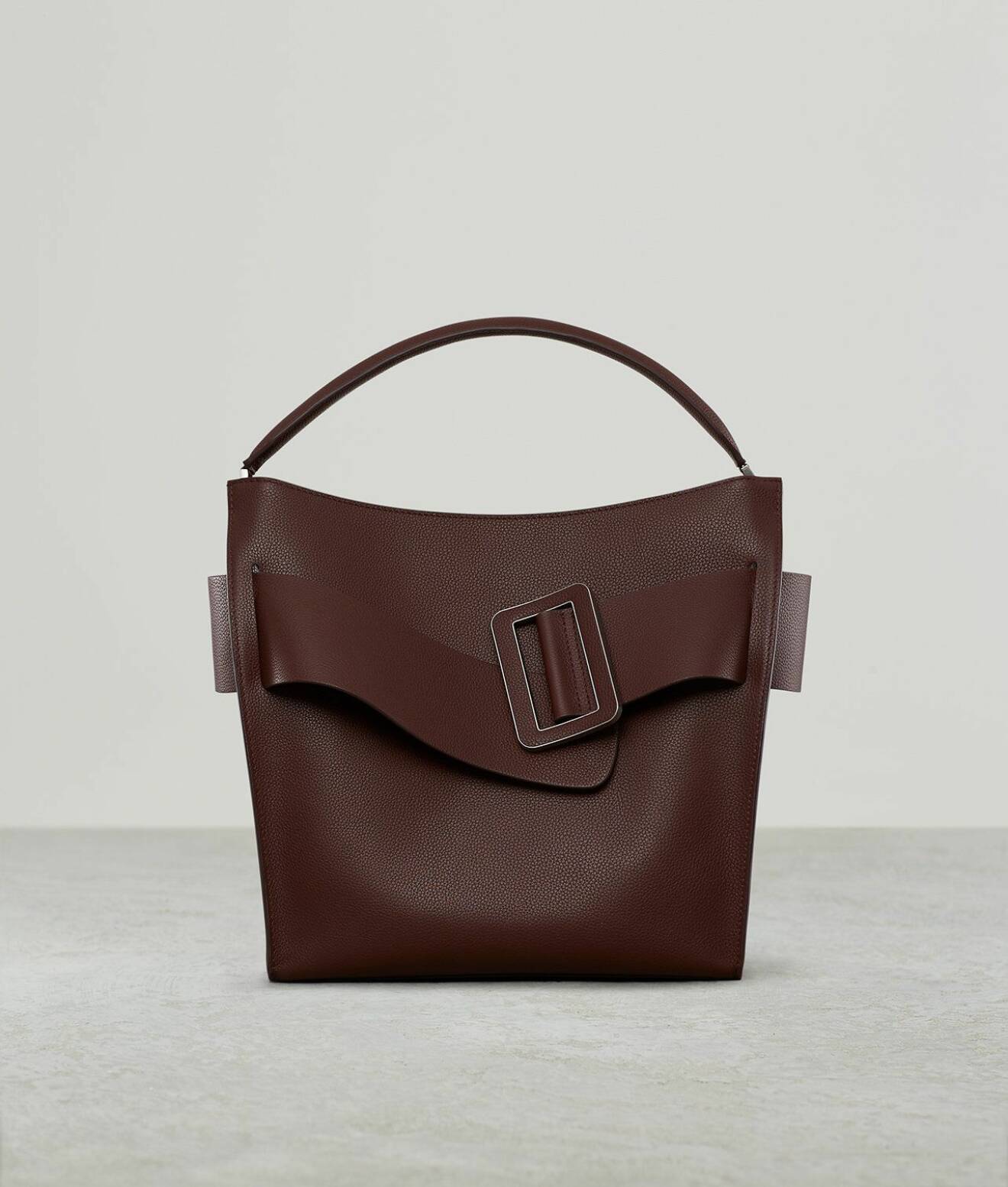 Skinnväska i brunrött med ett brett band med spänne över. Modellen heter "Pouch leather clutch" Väska i större modell från Boyy.