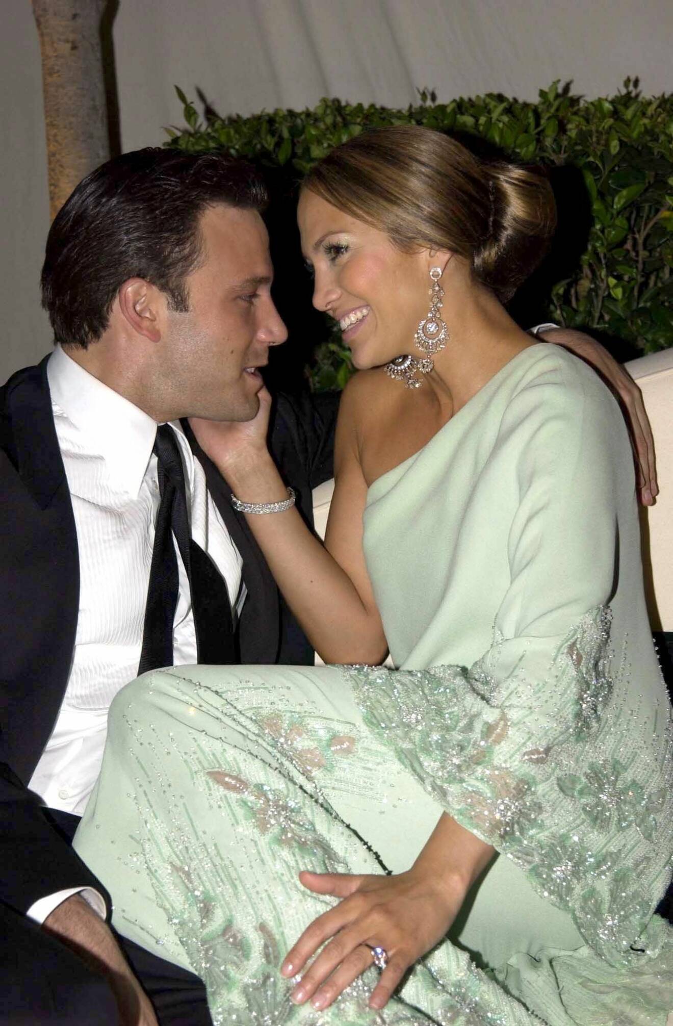 Jennifer Lopez och Ben Affleck sitter tillsammans uppkrupna i en soffa på en fest. Jennifer har en ljusrosa diamantring på vänstra fingret.