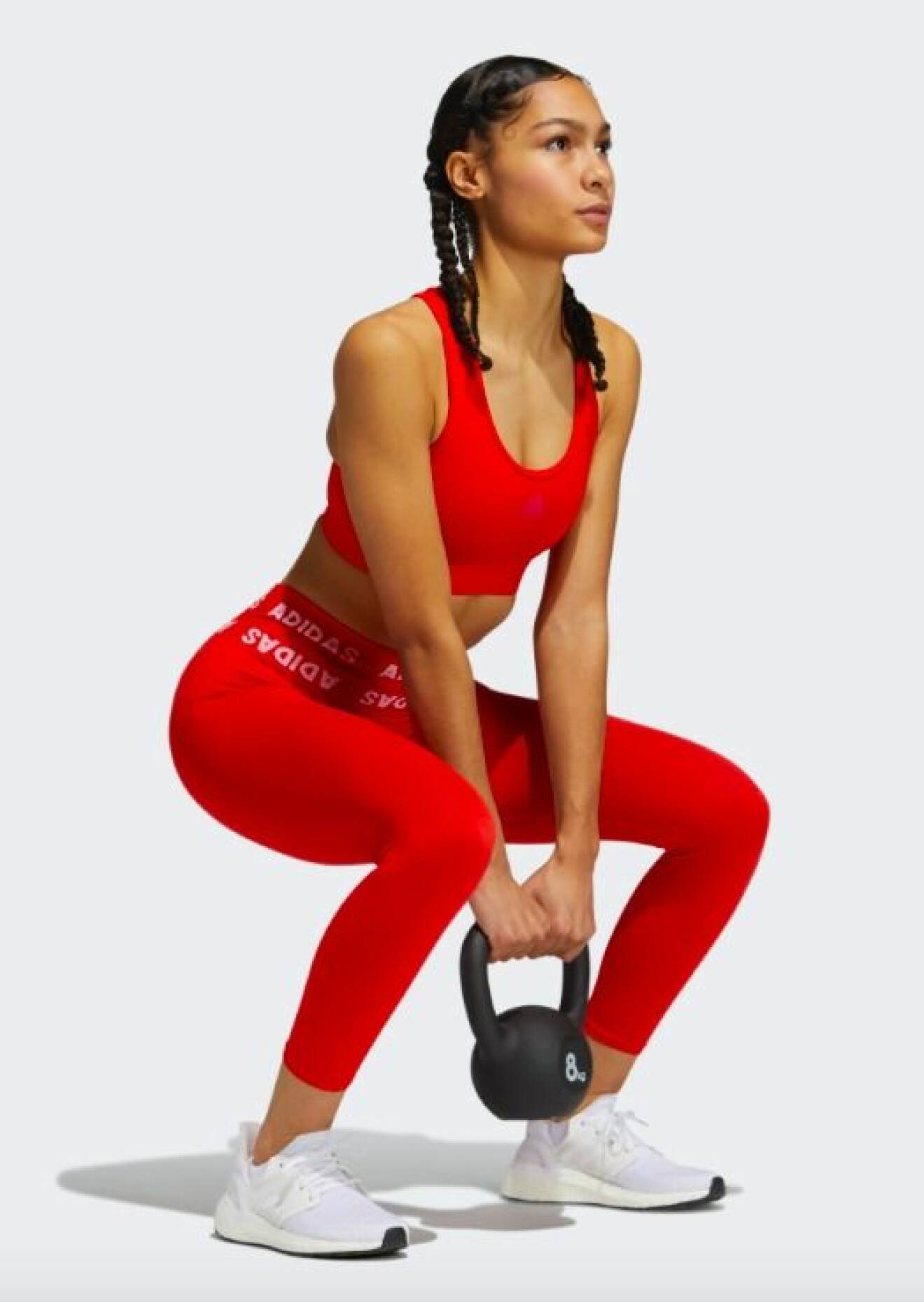 Modell med sporttopp och tights i knallrött från Adidas. Modellen lyfter en kettlebell på bilden.