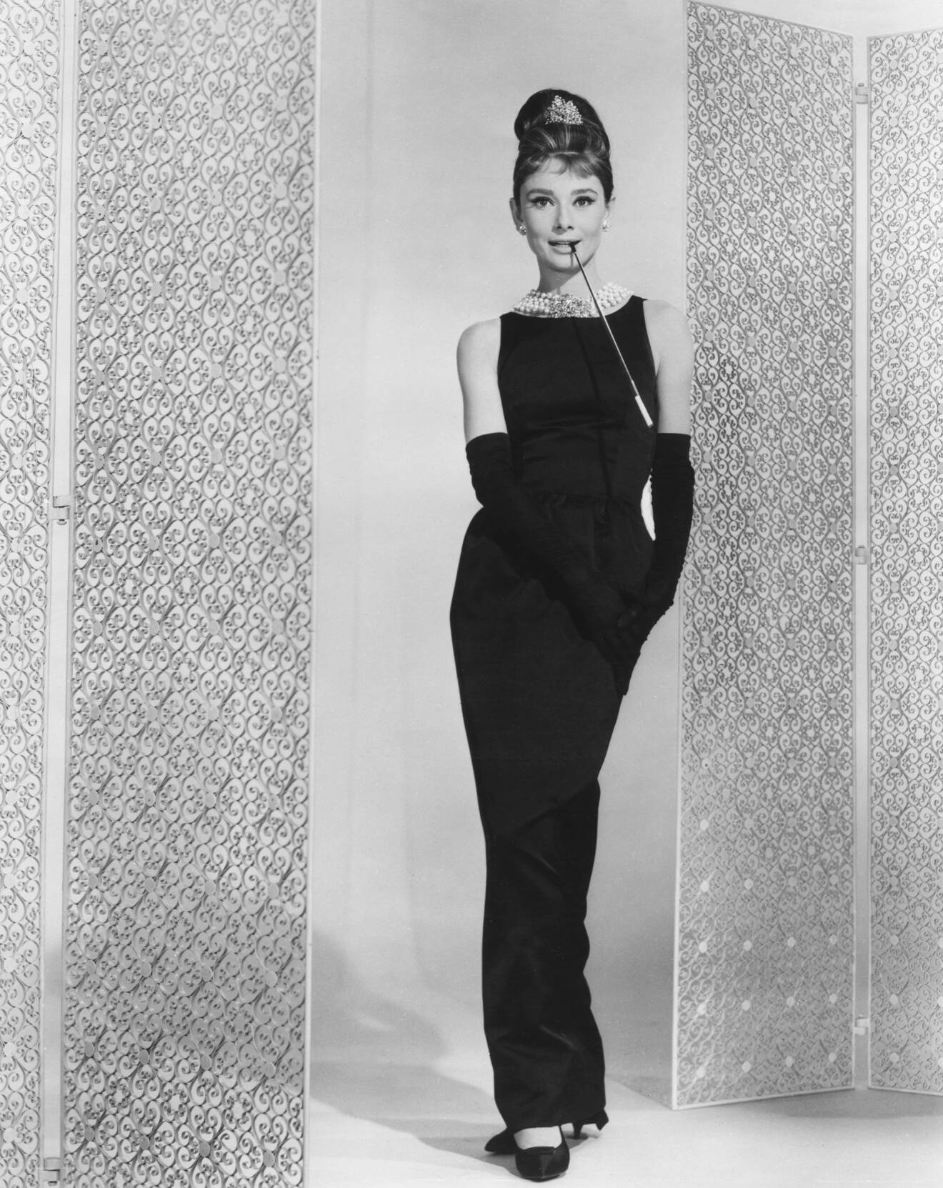 Audrey Hepburn i Breakfast at Tiffanys i ikonisk svart, fodralklänning och stort halsband runt halsen.