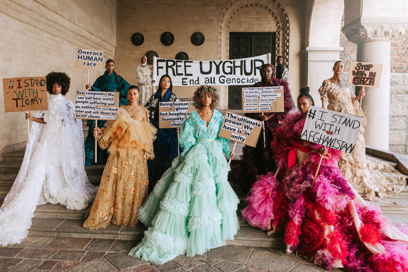 Gruppbild på modeller i stora, couture-klänningar i olika färger. Alla Modeller håller i plakat med budskap som "I stand with Afganistan", "Free Uyghur" och "Stop war in Gaza". Klänningarna är designade och sydda av designern Louise Xin. Foto av Emma Grann.