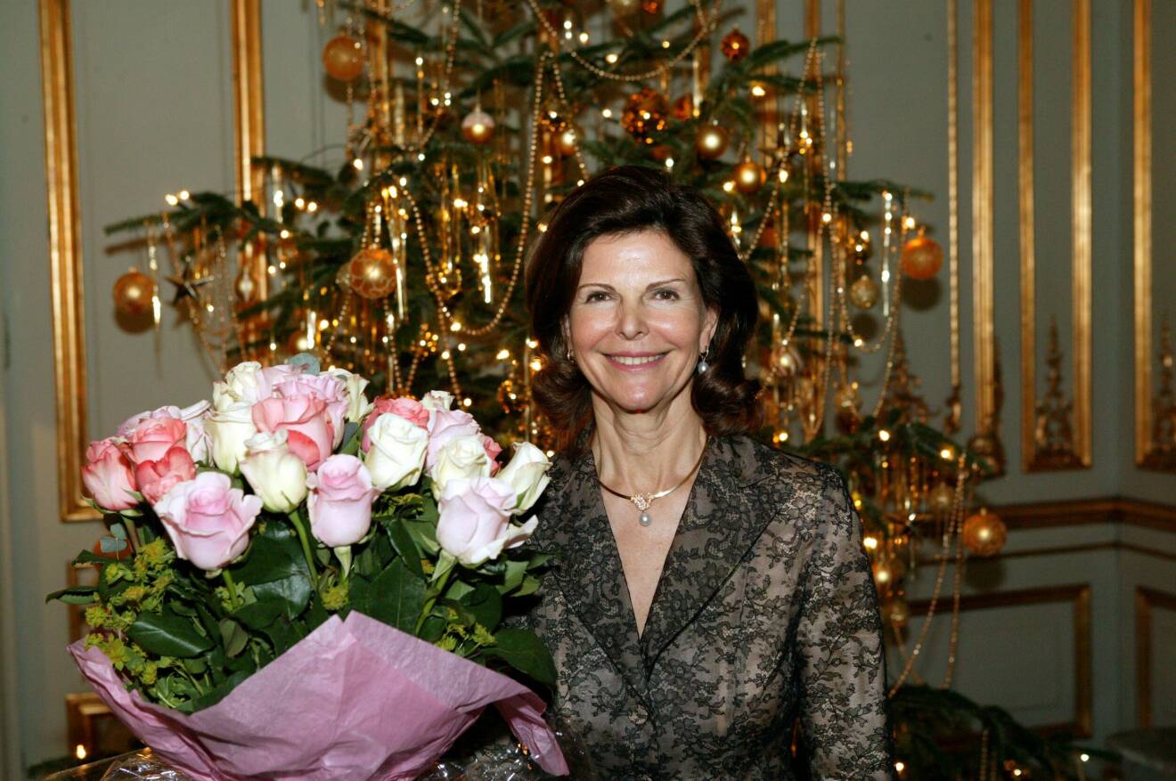 Drottning Silvia med en stor bukett blommor, framför julgranen på slottet.