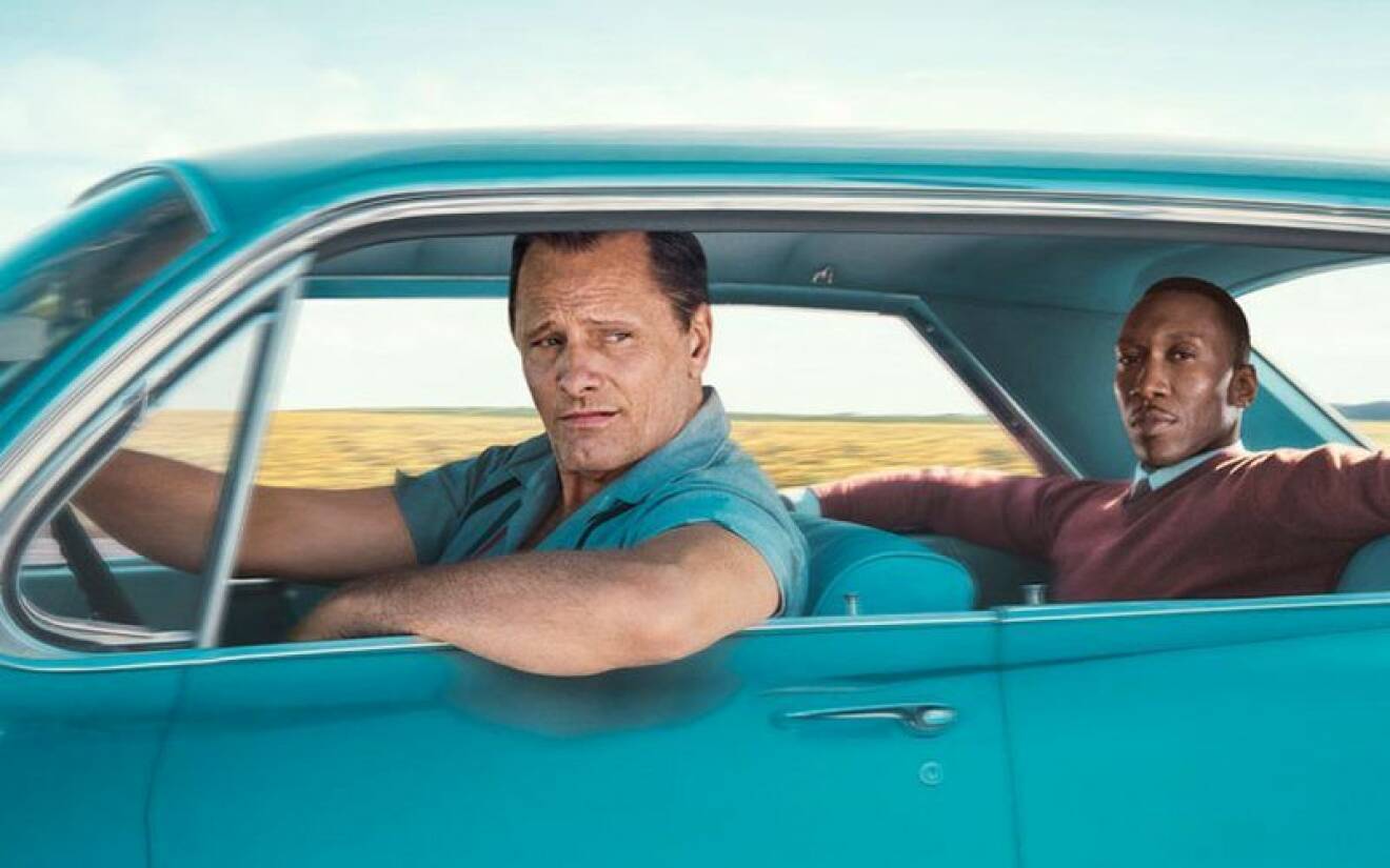 En man kör medan en annan sitter i baksätet i en blå bil.