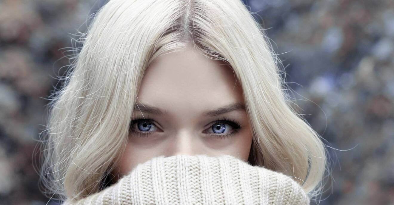 blond kvinna med isblå ögon som har tröjan uppdragen över munnen
