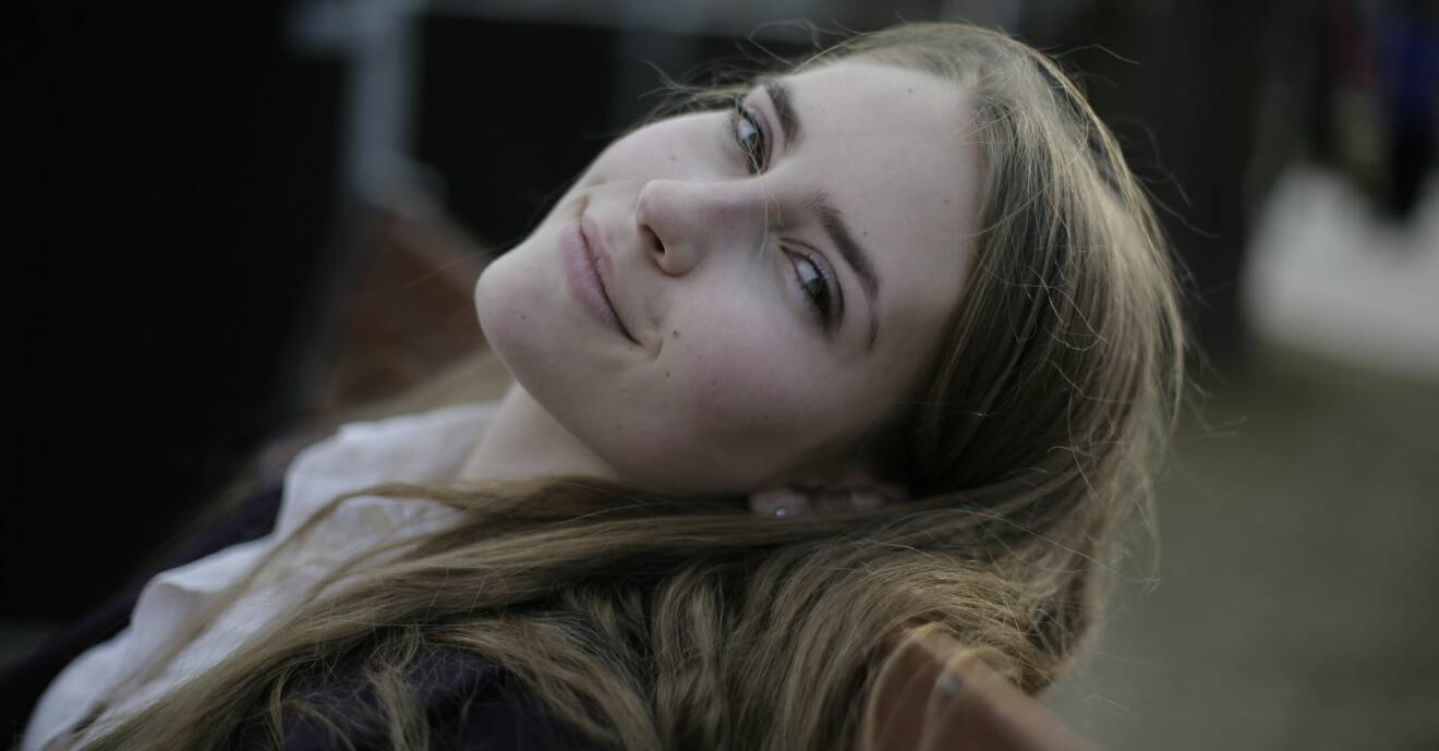 leende kvinna på parkbänk med långt brunblont hår