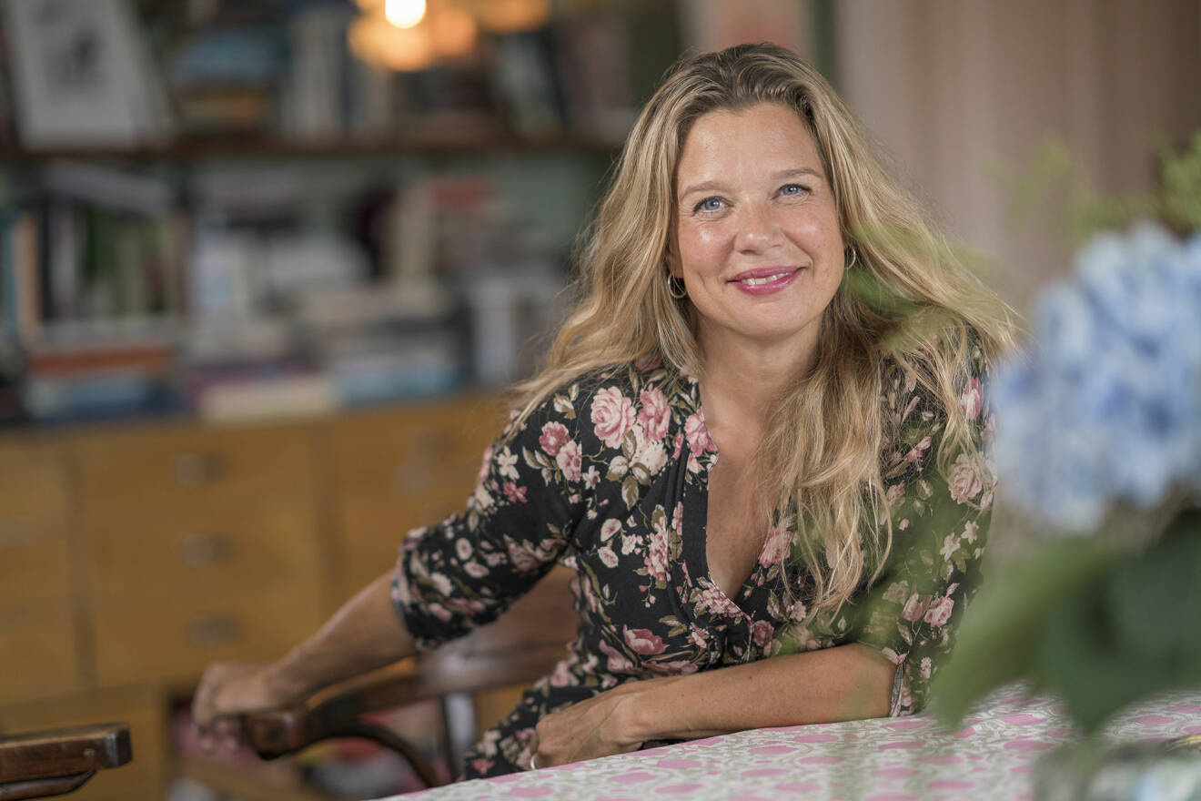 Författaren Emma Hamberg sitter vid ett bord och ler stort mot kameran. 