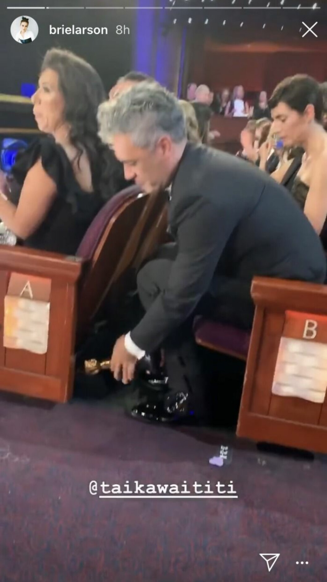 Taika Waititi gömmer sin Oscarsstatyett under stolen framför sig. taika waititi gömmer sin Oscarsstatyett under en stol