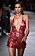 Modellen Irina Shayk på Versaces sommarvisning för 2020. En djupt v-ringad, kort klänning i rosa och rött med ett långt färgglatt strasshalsband som går ner i urringningen. Stora hoops med strass som matchar halsbandet.