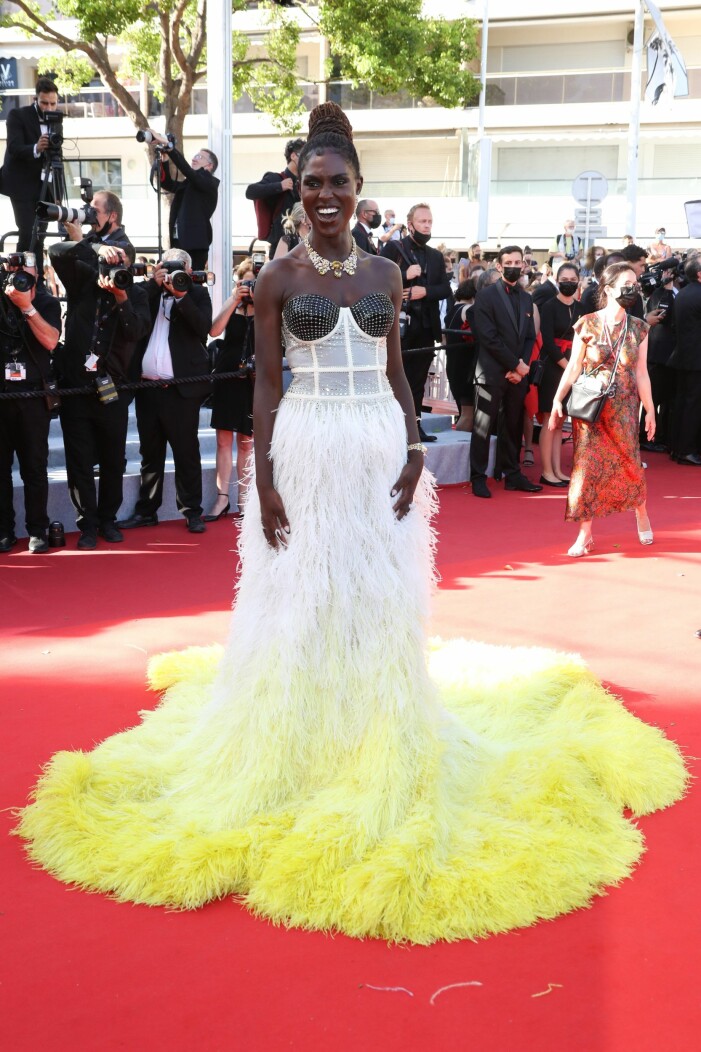 Jodie Turner-Smith. Foto: TT Jodie Turner-Smith i vit klänning med gul ombre nertill. Klänningen är gjord i fjädrar och har en korsett upptill i vitt med svart strass vid bysten.