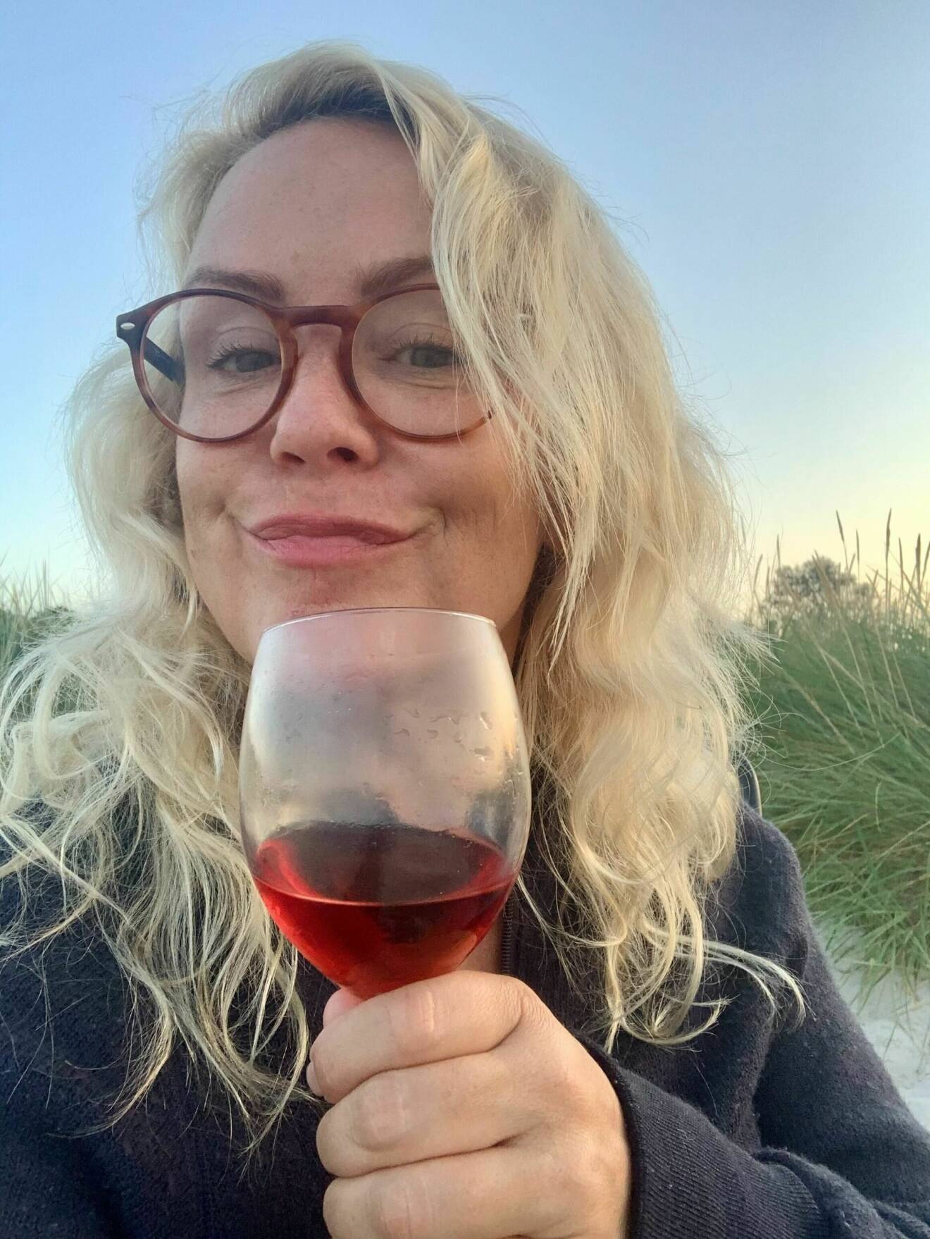 Karin Adelsköld dricker vin på en strand.