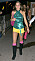Kate Middleton i en discoinspirerad outfit. Grön halternecktopp i paljett, rosa axelremsväska i skinn, gula, mycket korta shorts, rosa benvärmare under svarta boots som slutar strax under knäna.